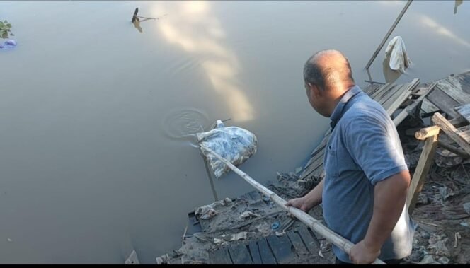 
 Warga mengangkat ikan busuk terbungkus plastik. foto-Haris